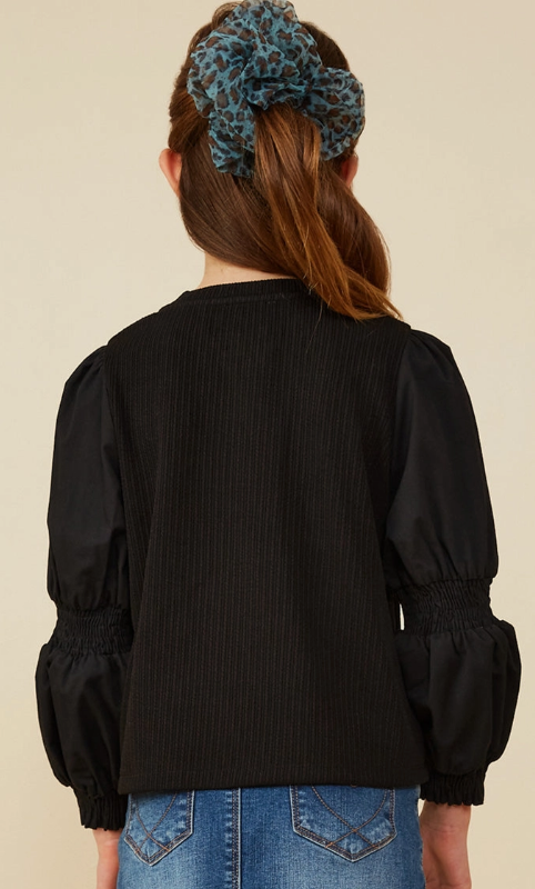 A girl with long brown hair in a blue leopard-print scrunchie is seen from the back, wearing the Hayden LA Puff Sleeve Textured Knit Top and blue denim jeans.