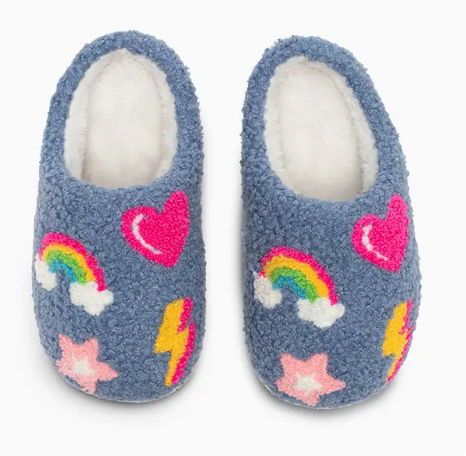 The Living Royal Rainbow Dreams Cozy Slippers are fluffy blue slippers with white interiors, decorated with colorful designs like pink hearts, rainbows, yellow lightning bolts, and pink stars.