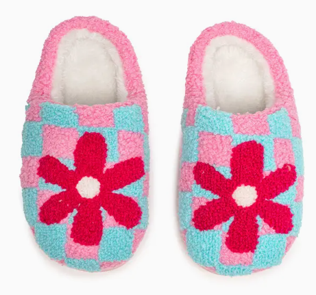 The Living Royal Flower Pop Checkered Slippers feature a blue and pink checkerboard pattern with bold red flowers on top, all set against a white background.
