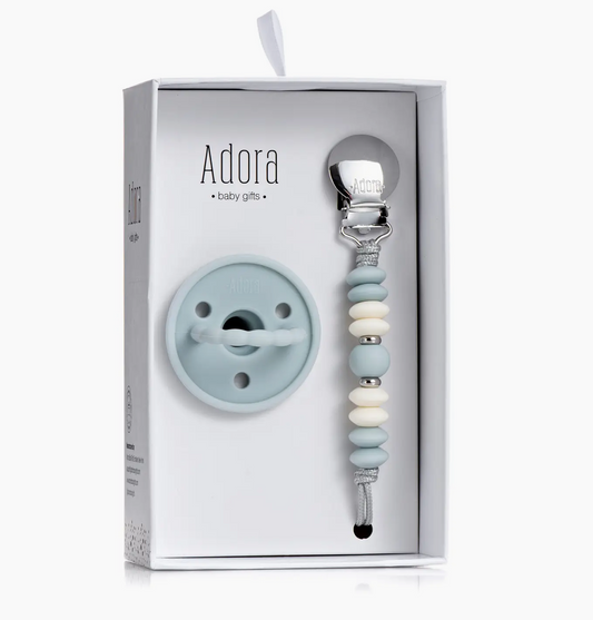 The Adora Classic Sky Vanilla Pacifier Clip Set includes a pale blue pacifier and a clip with blue, white, and gray silicone beads plus a silver clasp, all beautifully boxed in white packaging.