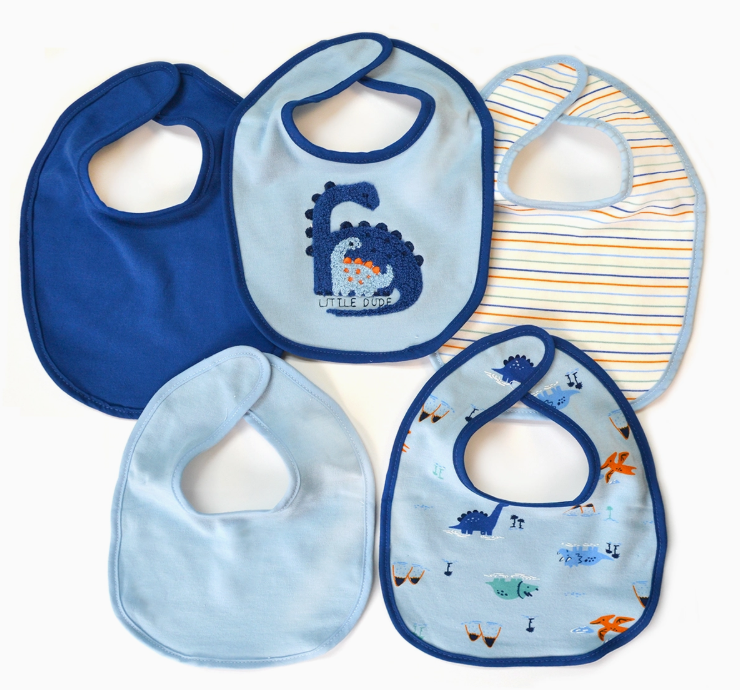 Five baby bibs from the Lollipop Dreams Little Dude Dino Bib Set are arranged in a circle: one with a dinosaur, one with ocean animals, one striped, and two solid blue shades.