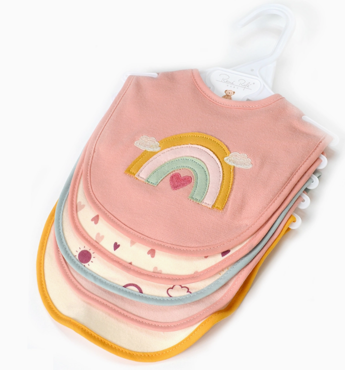 The Rainbow Dreams Bib Set by Lollipop Dreams includes four colorful baby bibs on a hanger, with the top bib showcasing a rainbow and heart on pink, and the others featuring pastel borders and simple patterns.