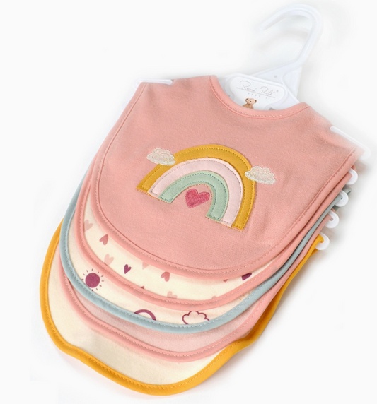 The Rainbow Dreams Bib Set by Lollipop Dreams includes four colorful baby bibs on a hanger, with the top bib showcasing a rainbow and heart on pink, and the others featuring pastel borders and simple patterns.