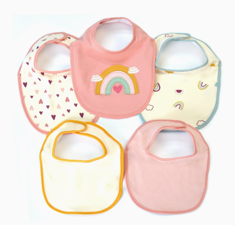 The Rainbow Dreams Bib Set by Lollipop Dreams displays five baby bibs in a semi-circle, featuring pastel pink, yellow, and white solids plus heart, rainbow, and cloud patterns with colorful trim or embroidered details.