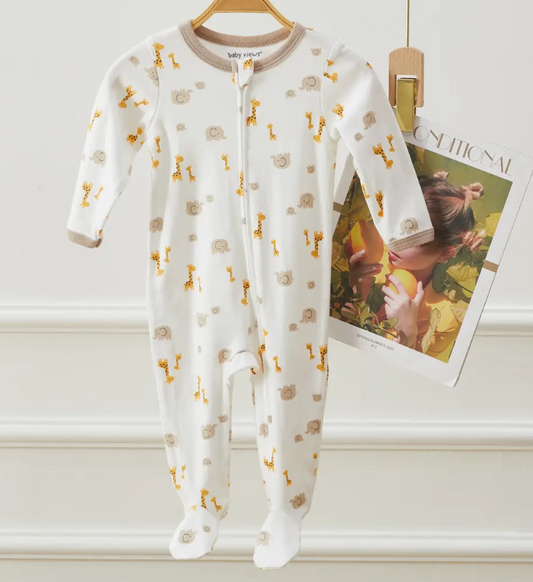 The Lollipop Dreams Safari Friends Zip Footie, a white baby onesie with brown trim featuring yellow giraffe and gray elephant prints, hangs on a wooden hanger next to a clipped magazine.