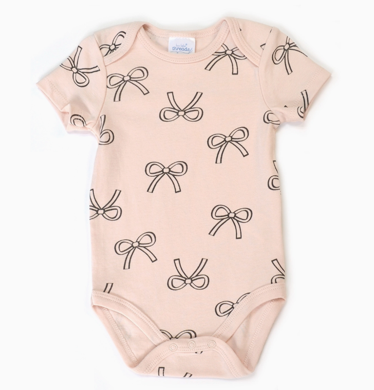 The Cherry Bow Bubble Trio by Lollipop Dreams is a light pink short-sleeve baby onesie, decorated with a playful pattern of simple black outlined bows across the fabric.