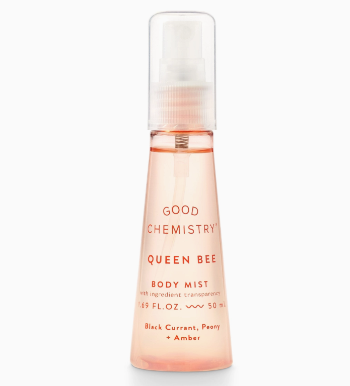A 50 mL clear spray bottle labeled Good Chemistry Queen Bee Mini Body Mist holds pink liquid; this floral scent blends sparkling fruits, black currant, peony, and amber notes.