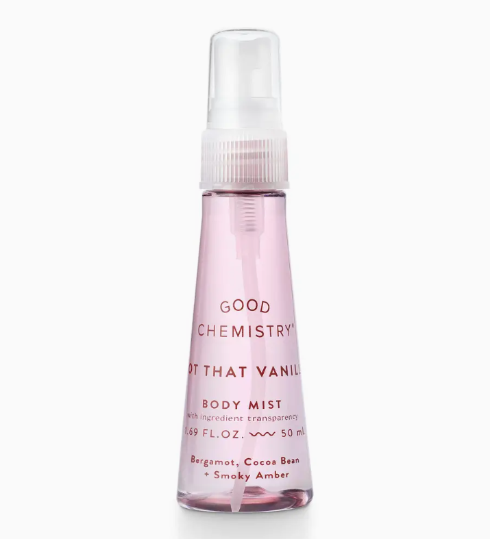 A clear plastic mini spray bottle of Good Chemistry’s Not That Vanilla Body Mist with pink liquid, featuring a white cap. The label notes bergamot, cocoa bean, and smoky amber fragrances.