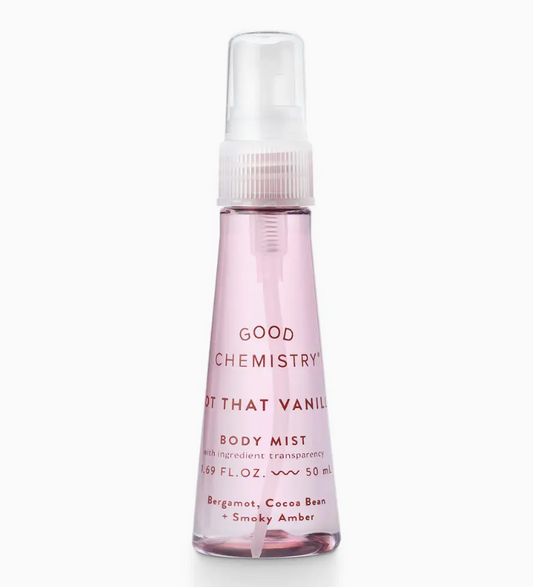 A clear plastic mini spray bottle of Good Chemistry’s Not That Vanilla Body Mist with pink liquid, featuring a white cap. The label notes bergamot, cocoa bean, and smoky amber fragrances.