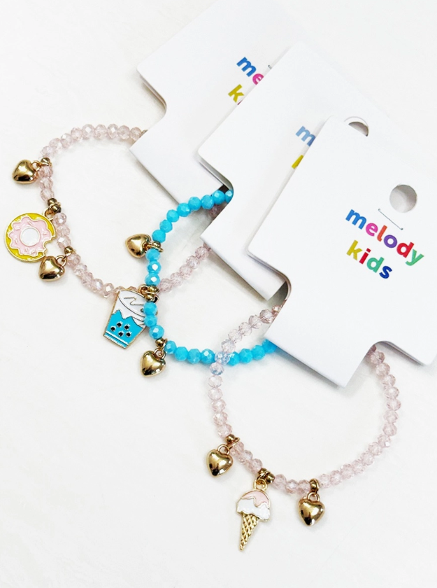 Two love & repeat Sweet Treat Charm Bracelets for kids, each with gold heart charms and colorful enamel donut, drink, and ice cream cone charms, displayed on white melody kids cards.