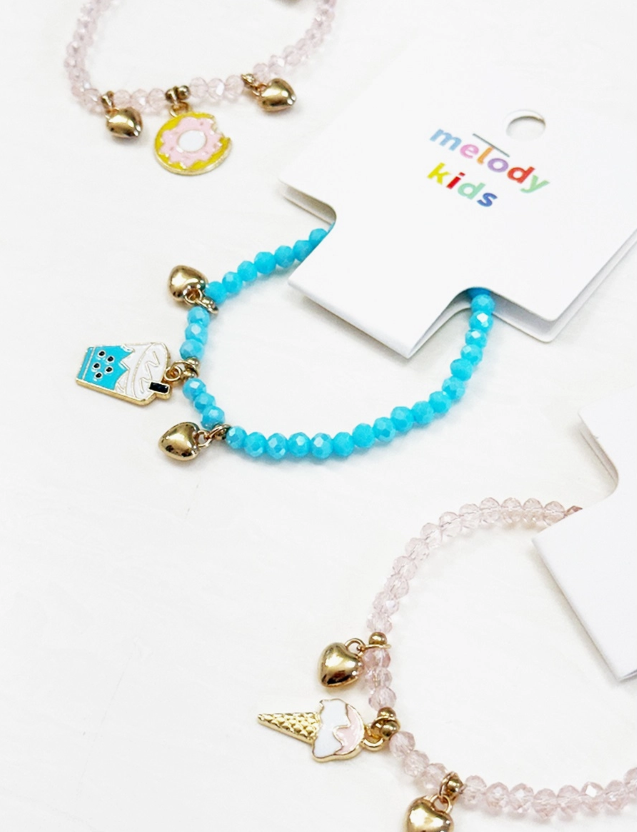 Three Sweet Treat Charm Bracelets by love & repeat are shown: one blue with a sheep charm, two pink with ice cream and donut charms, each featuring gold heart accents and a melody kids tag.