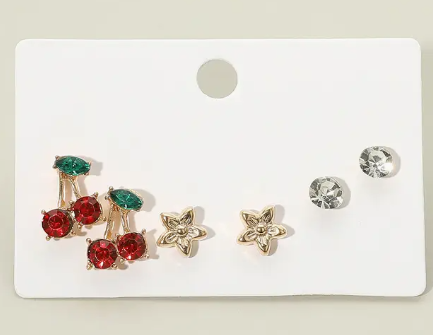 A white card displays the Sensibling Corp. Tiny Sparkle Stud Trio: gold and red earrings with green stones, gold flower-shaped studs, and simple round clear studs.