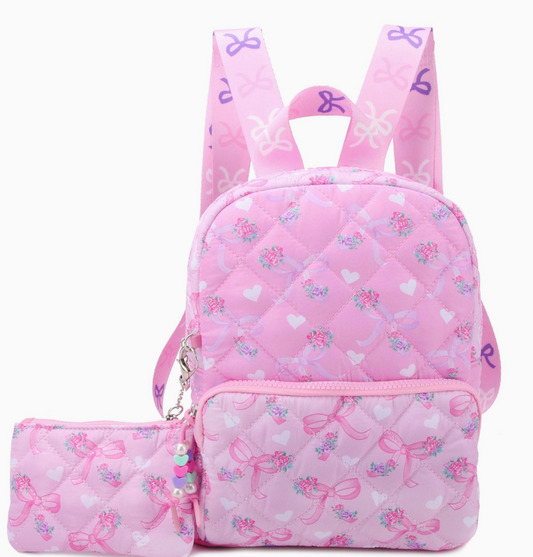 The omg Accessories Sweetheart Bows Quilted Backpack is a small pink backpack with a matching coin purse, both featuring ballet shoes, pink ribbons, hearts, and flower bouquets. The straps have purple and pink bow designs.