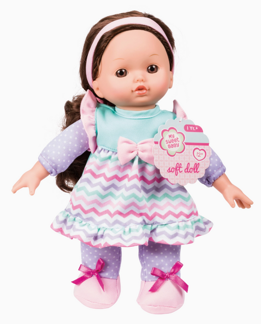 The Tiny Tot Bundles Sweet Baby 12" Soft Bodied Doll features brown hair, a pink headband, pastel zigzag dress, purple polka-dot sleeves and pants, and pink shoes with bows. Suitable for ages 12+ months.