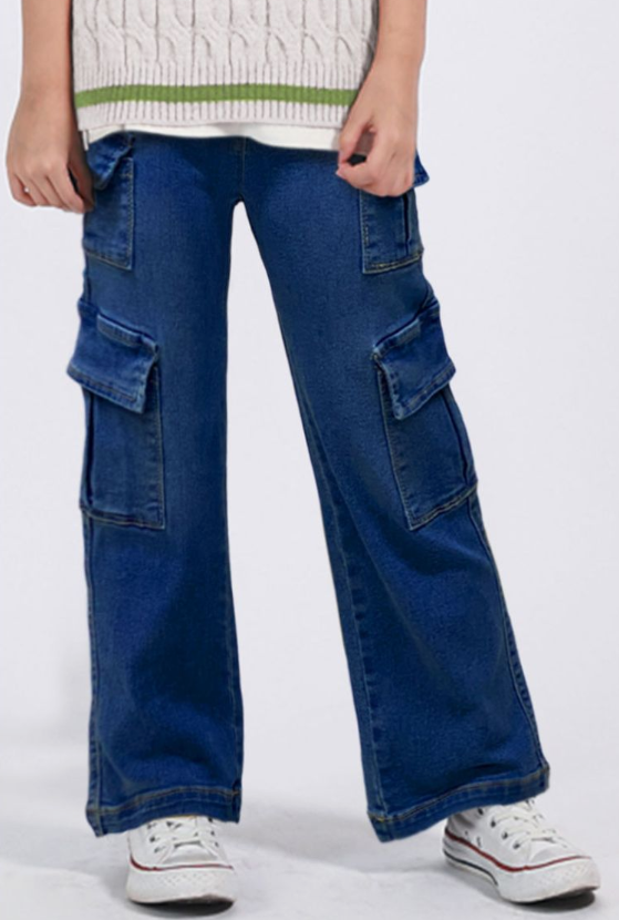 A person models Cutie Patootie Girls Dark Denim Jeans, styled with a cream sweater featuring green trim and white sneakers. The photo captures them from the shoulders down, highlighting the trendy wide-leg design and side pockets.