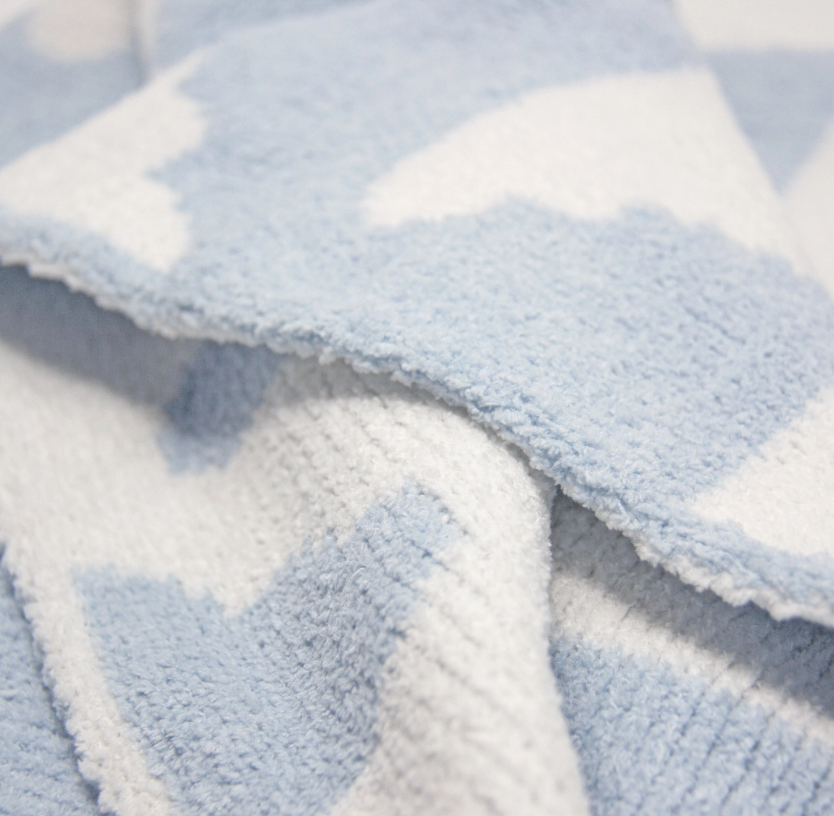 Close-up of the living textiles Chenille Baby Blanket - Blue Clouds, highlighting its soft, fluffy texture and light blue and white cloud pattern.