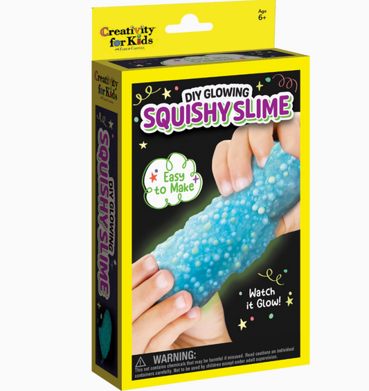 A box of Diy Glowing Squishy Slime Mini Kit by Creativity For Kids is shown with hands squeezing blue beaded slime. The yellow and black packaging features "Easy to Make" and "Watch it Glow!" phrases and suits ages 6+.