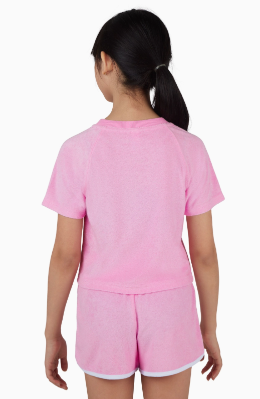 A young girl with dark ponytail is seen from behind, wearing the Cotton Candy Towel Terry Short Set by 90 Degree by Reflex & Yogalicious—a light pink short-sleeve top and matching shorts—against a white background.