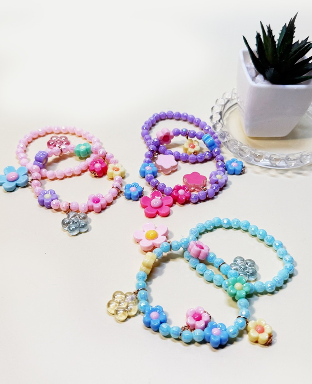 The funteze Flower Mix Bead Layered Bracelets in pastel pink, purple, and blue with flower charms are displayed on a white surface next to a small potted succulent in a white planter.