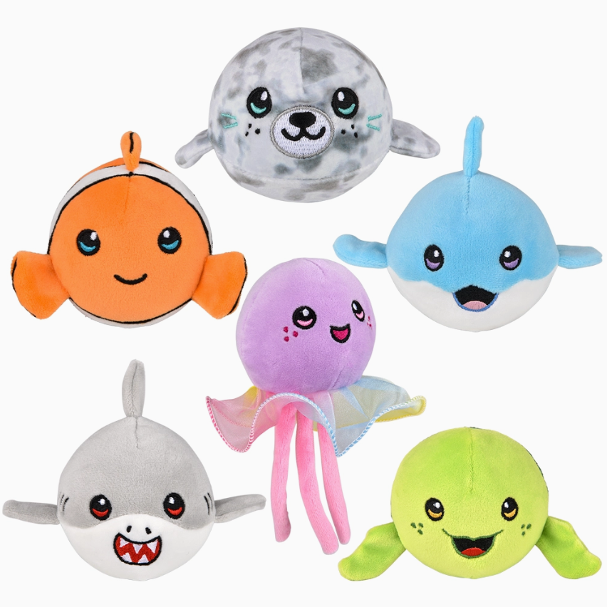 Tumble Tykes Sea Life by Tiny Tot Bundles features six colorful plush sea animals with smiling faces, including a clownfish, seal, dolphin, shark, pink-tentacled octopus, and light green fish against a white background.