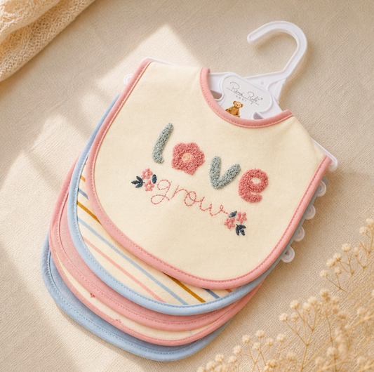 The Sweetheart Baby Bib Set by Lollipop Dreams features pastel bibs—pink, yellow, blue, and striped—on a hanger. The top bib is embroidered with "love grow" and small floral designs for a charming touch.