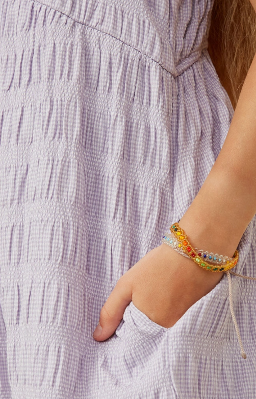 A person wearing the Hayden LA Purple Bow Tank Romper with their hand in the pocket, showing colorful beaded bracelets and long brown hair.