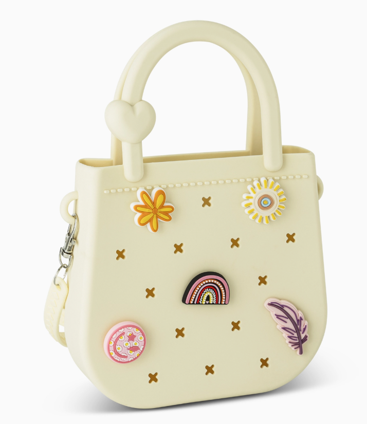 The Mini Round Eva Set Purse by core home is a small, light yellow handbag featuring a heart detail on the handle and decorated with colorful pins such as a flower, rainbow, doughnut, daisy, and feather.