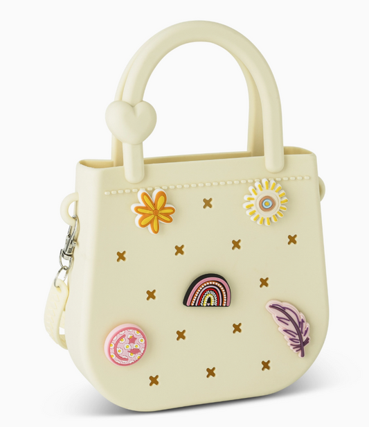The Mini Round Eva Set Purse by core home is a small, light yellow handbag featuring a heart detail on the handle and decorated with colorful pins such as a flower, rainbow, doughnut, daisy, and feather.