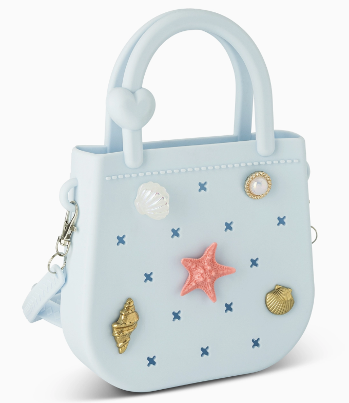 The core home Mini Round Eva Purse - Blue is a small, light blue handbag with a heart-shaped handle and sea-themed charms—starfish, shells, and pearl—plus a detachable side strap.