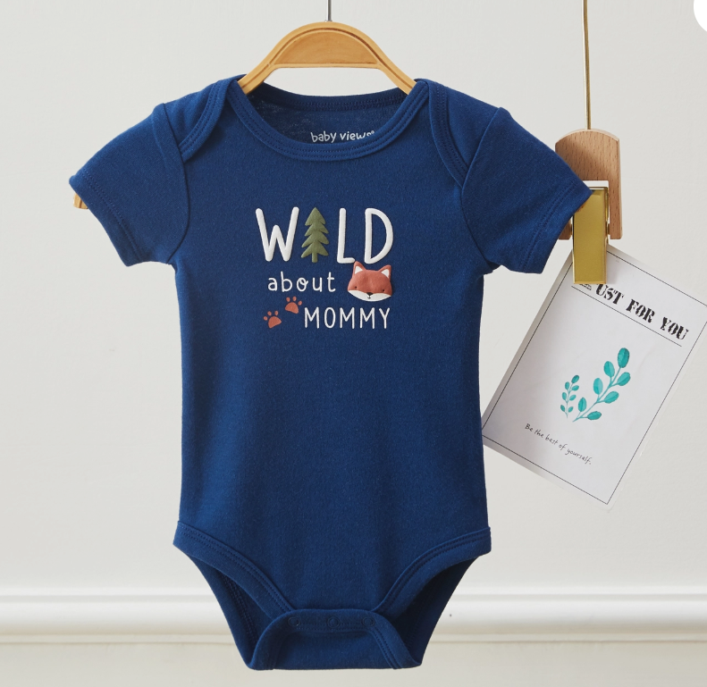 The Lollipop Dreams Wild About Mommy Bubble Trio, a blue baby onesie with “WILD about MOMMY,” features a fox and tree illustration. Displayed on a wooden hanger, it’s shown beside a card with plant-themed art.