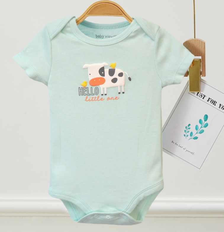 Light green Tiny Farm Bubble Trio onesie by Lollipop Dreams hangs on a wooden hanger, featuring a cartoon cow with yellow birds and "HELLO little one" on the chest. A tag with a plant illustration is attached beside it.