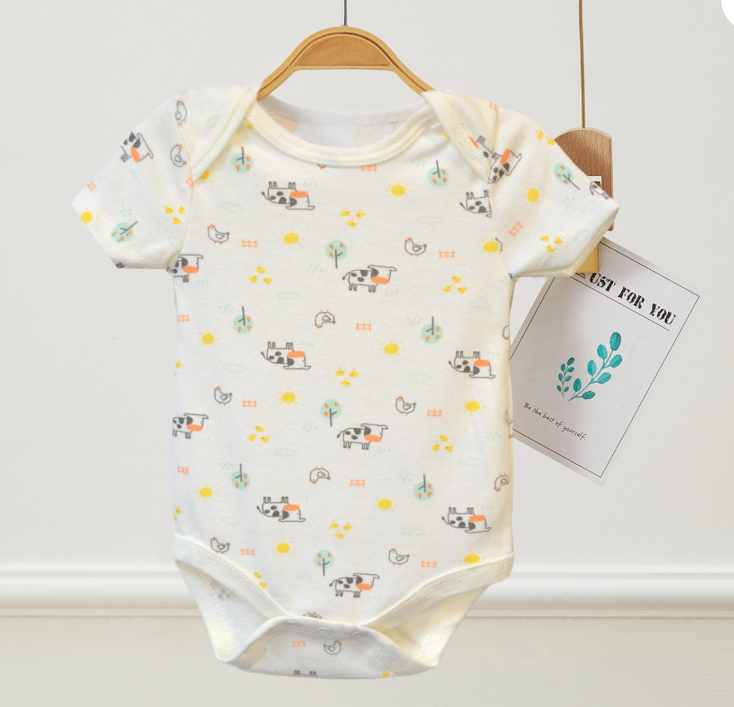 The Tiny Farm Bubble Trio by Lollipop Dreams is a white short-sleeve baby onesie with colorful farm prints of cows, chickens, trees, and suns, displayed on a wooden hanger with an attached tag.