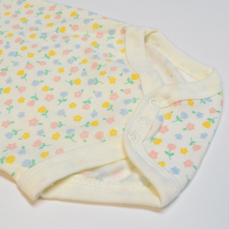A close-up of the Lollipop Dreams Mommy’s Mini Bubble Trio onesie, featuring a pastel floral pattern in pink, yellow, and blue with white trim and three bottom snaps.