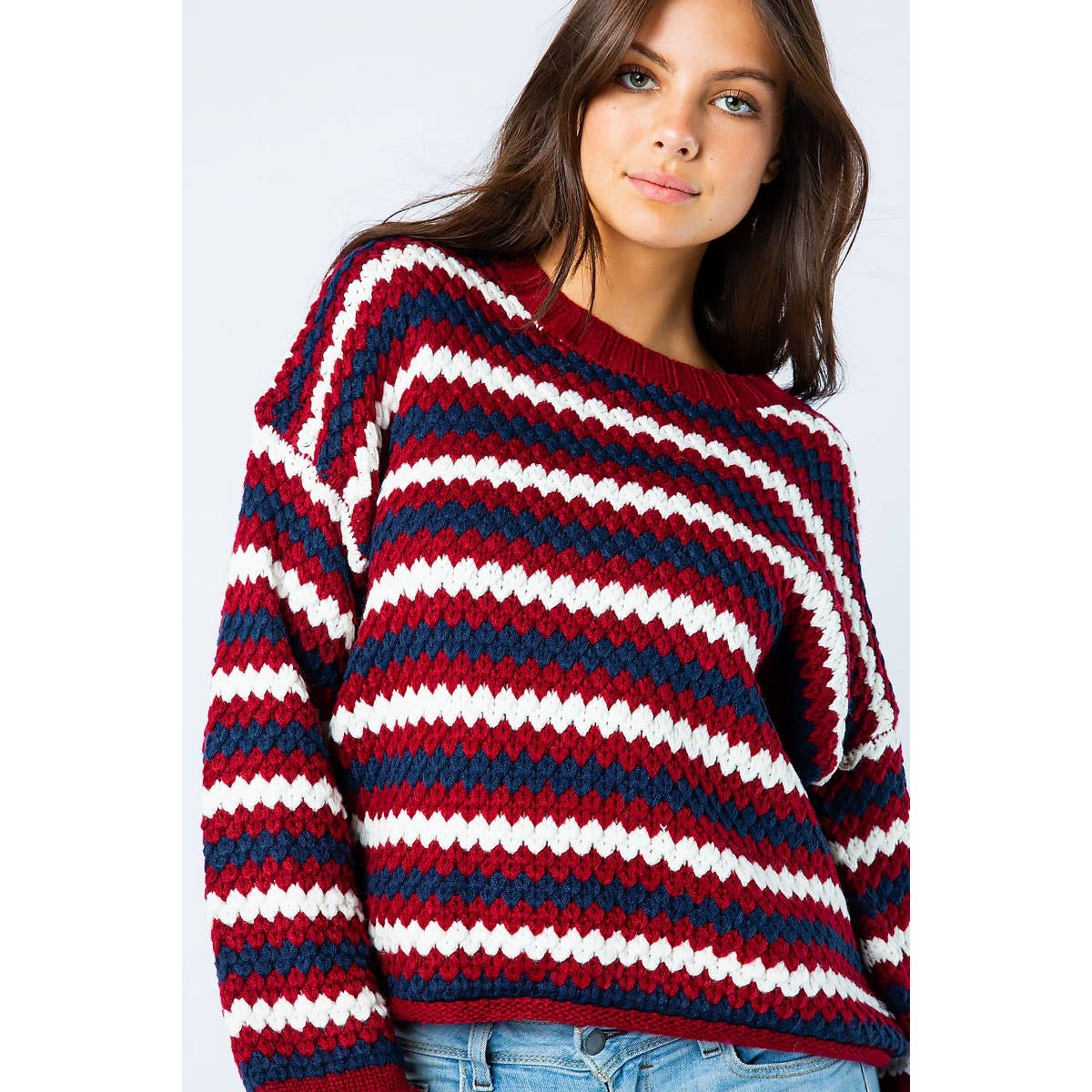 A woman wears a Sweet Generis Chunky Knit Multi Color Sweater featuring horizontal stripes in red, navy blue, and white.
