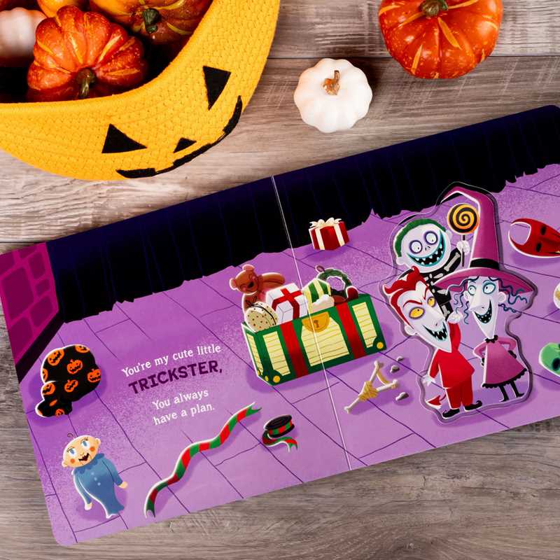 The Simon & Schuster children’s book “You’re My Little Nightmare” by Grace Baranowski is open on a table, featuring cartoon characters on stage. Nearby are a yellow jack-o-lantern bowl, small pumpkins, and Halloween candy.