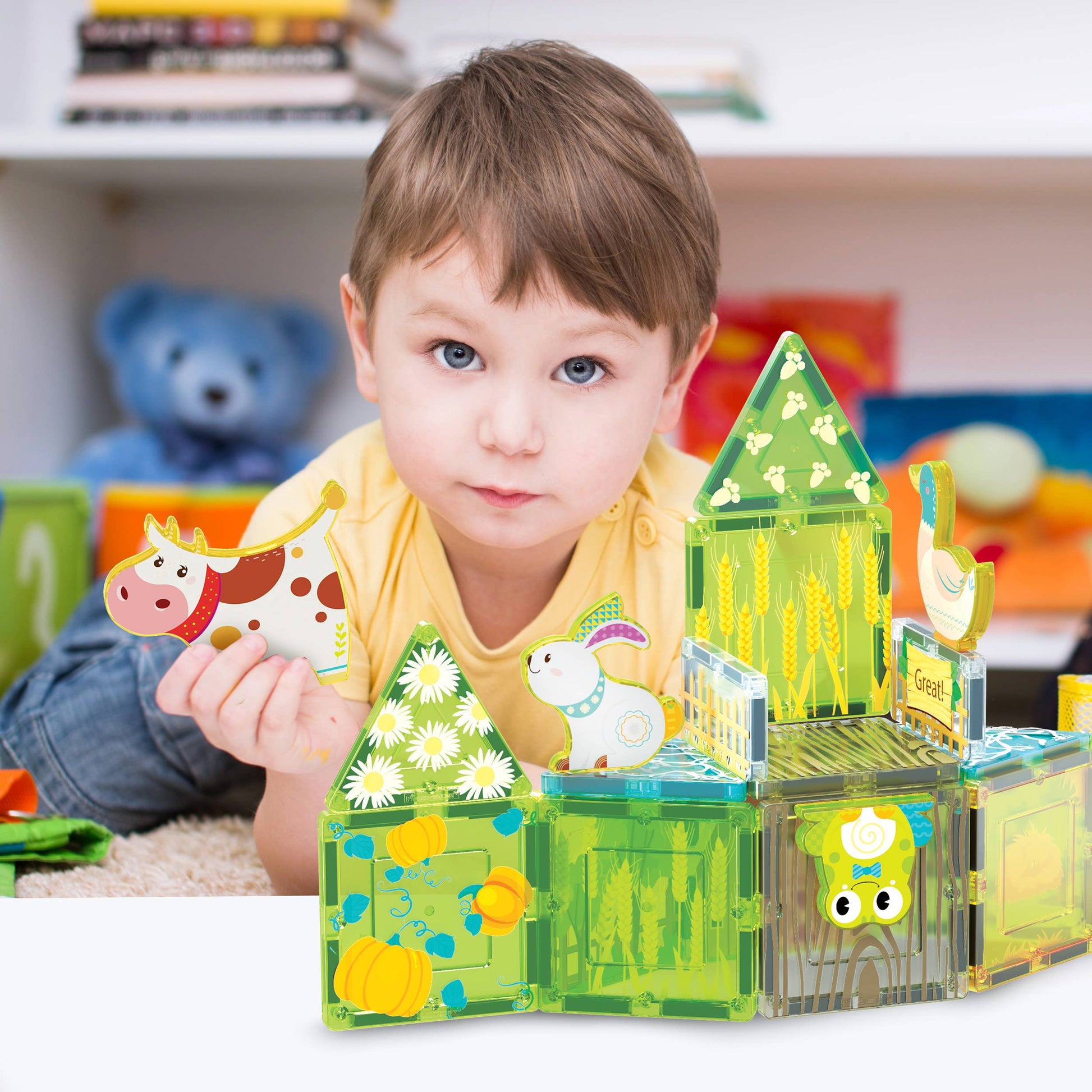 A young child with short brown hair plays in a cozy playroom with the PicassoTiles 26pc Magnetic Tile Farm Theme Toy Set PTQ27 by PicassoTiles, building colorful structures and playing with farm animal figures like a cow and bunny.