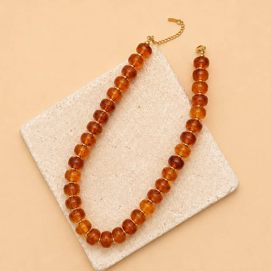 JOSSLYN by wall to wall Chunky Amber-Tone Barrel Bead Necklace featuring a single strand of translucent, amber-toned barrel-shaped beads with gold-tone spacers and a lobster clasp.