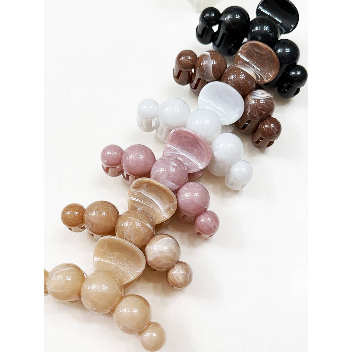 Five Love and Repeat Large Marbled Hair Claws in shades of black, brown, white, pink, and beige are arranged in a row on a white surface.