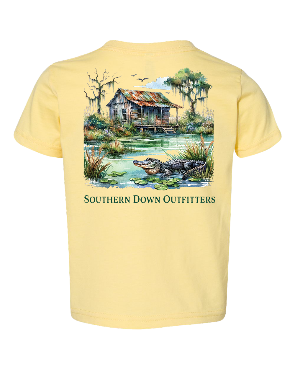 The Swamp Shack Toddler Tee by Southern Down Outfitters is a light yellow t-shirt with an alligator illustration by a pond, old wooden cabin, trees, and birds. Features "SOUTHERN DOWN OUTFITTERS" text.