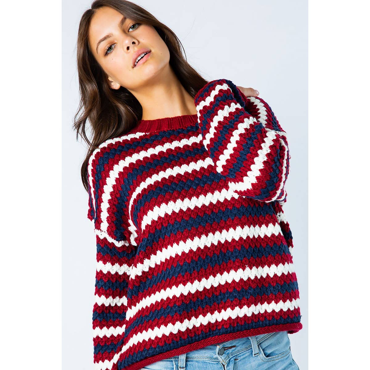 A person wears a Sweet Generis Chunky Knit Multi Color Sweater, featuring a long-sleeved, chunky knit design with horizontal stripes in red, white, and navy blue.