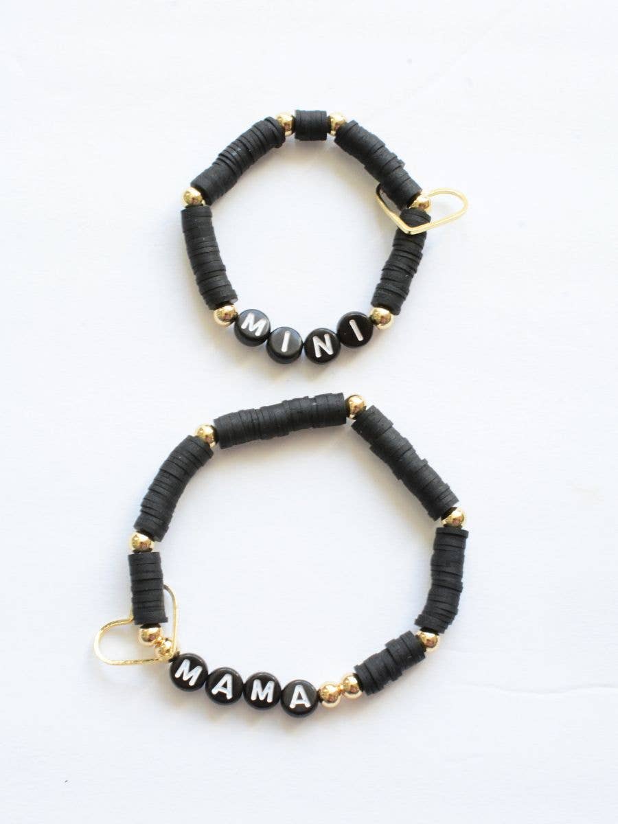 Set of two beaded bracelets from Two and Crew - Faith Based Jewelry & Gifts, called the Mama Mini Bracelet Set - Black. Each bracelet features black beads with gold accents; one is lettered “MINI” with white letter beads, the other spells “MAMA.” Both are displayed on a white background.