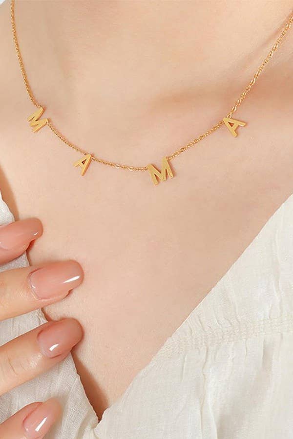 A close-up of the Mama Tarnish Free Necklace by JOSSLYN by wall to wall, worn by a person in a white top with their hand resting on their chest, showcasing nude-colored nail polish.