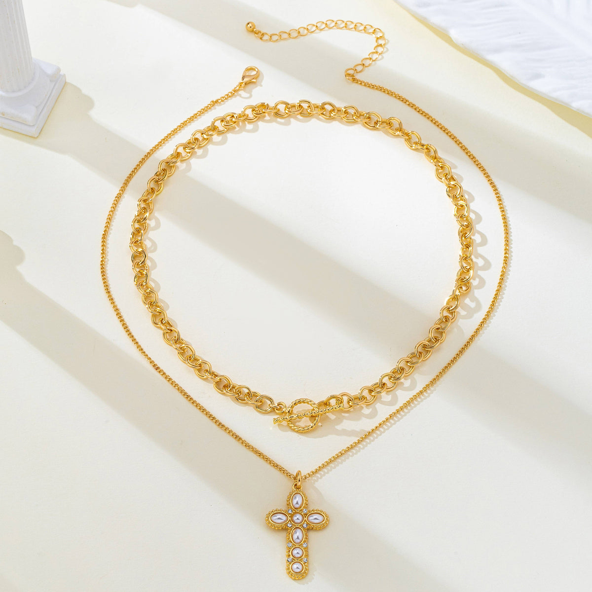 JOSSLYN by wall to wall Pearl Cross Layered Necklace Set featuring a thick gold-toned chain with a toggle clasp and a delicate chain with a cross pendant inlaid with small white pearls and crystals.