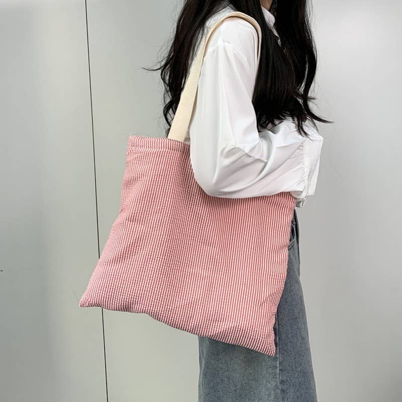 A person wearing a white shirt and denim skirt carries a JOSSLYN by wall to wall Large Red Stripe Shoulder Tote Bag featuring red and white stripes and cream-colored shoulder straps.