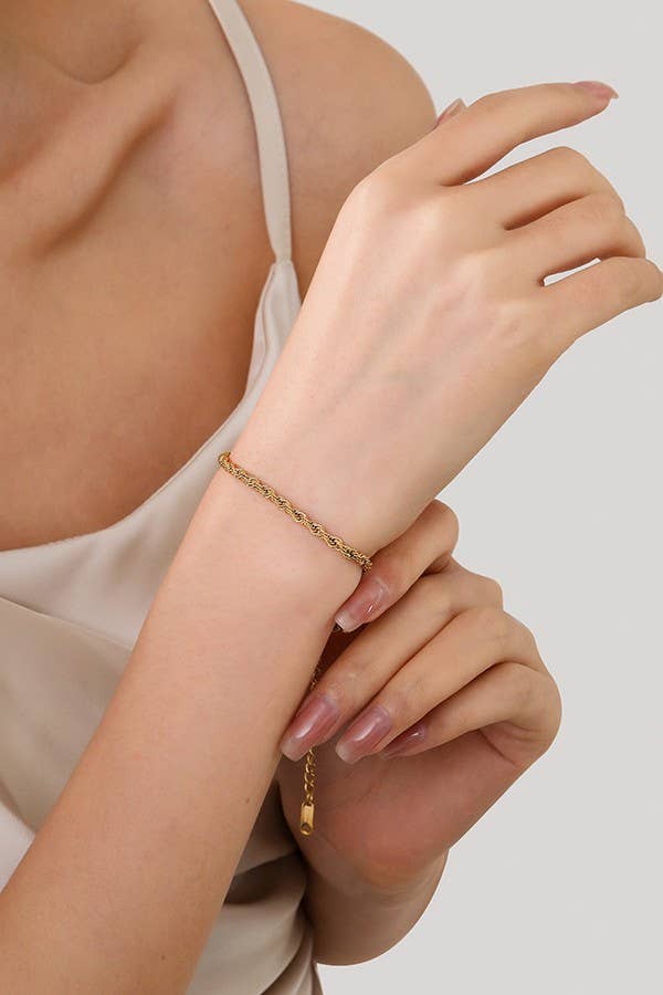 A woman models the JOSSLYN by wall to wall Dainty Gold Bracelet on her wrist, elegantly dressed in a beige satin camisole and gently holding her arm with her opposite hand against a neutral background.