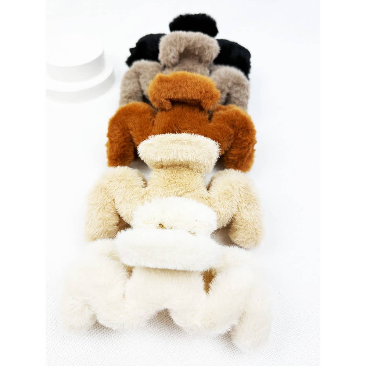 Four Love and Repeat Jumbo Fur Wavy Hair Claw Clips in cream, beige, brown, and black are arranged in a row on a white surface, each clip facing the same direction.