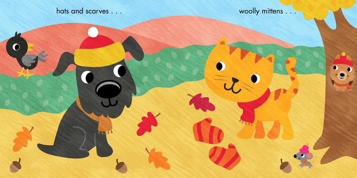 A charming illustration from the Fall Is Here! Book by Simon & Schuster features a cartoon dog wearing a hat and scarf sitting next to a cat in a red scarf, surrounded by woolly mittens, autumn leaves, a bird, tree, and squirrel in a cozy fall setting. Text reads: hats and scarves . . . woolly mittens . . ..