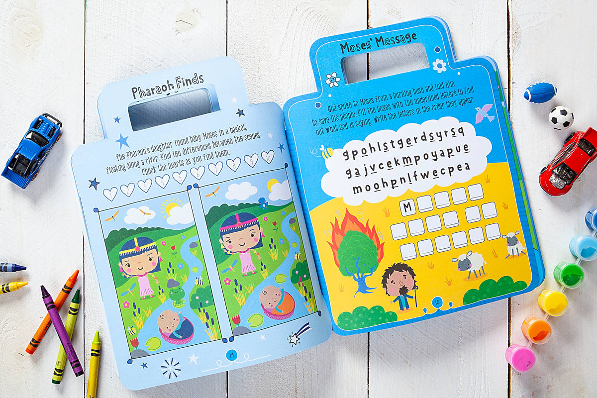 A copy of the “My Bible Backpack Activity Book” by BroadStreet Publishing Group, LLC is open to pages filled with colorful spot-the-difference and word puzzle games, surrounded by crayons, small toy cars, balls, and a die on a white wooden surface.