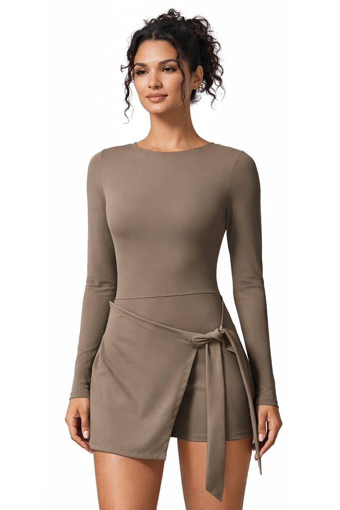 A woman wearing the Color 5 Mocha Long Sleeve Athletic Dress, featuring a round neckline and a wrap-style skirt tied at the waist, stands against a white background.