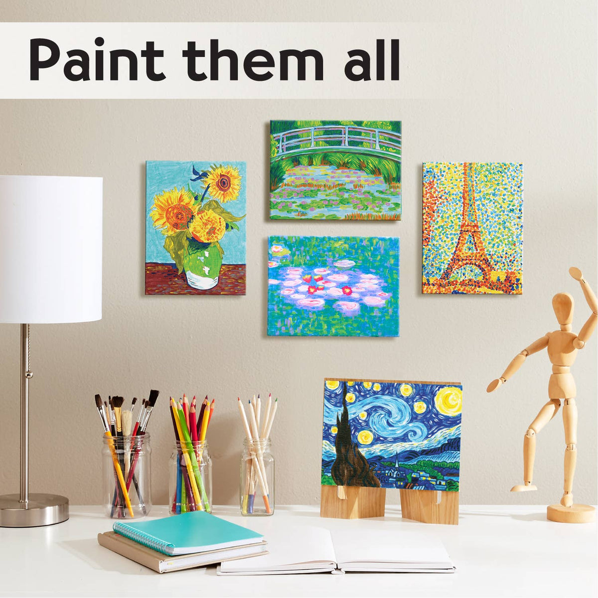 A desk featuring the Paint by Number Museum Series - The Japanese Footbridge by Faber-Castell / Creativity for Kids is set with art supplies, a lamp, a wooden mannequin, and an artist canvas showcasing miniature masterpieces—including The Japanese Footbridge—with the words “Paint them all” above, inspiring you to paint like the Masters.